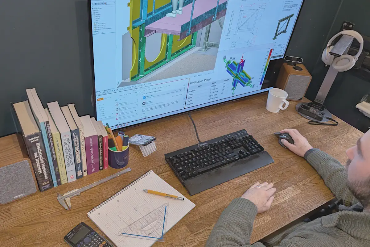 Engineer working at a desk with 3D CAD, FEA and emails on screen during focused design development